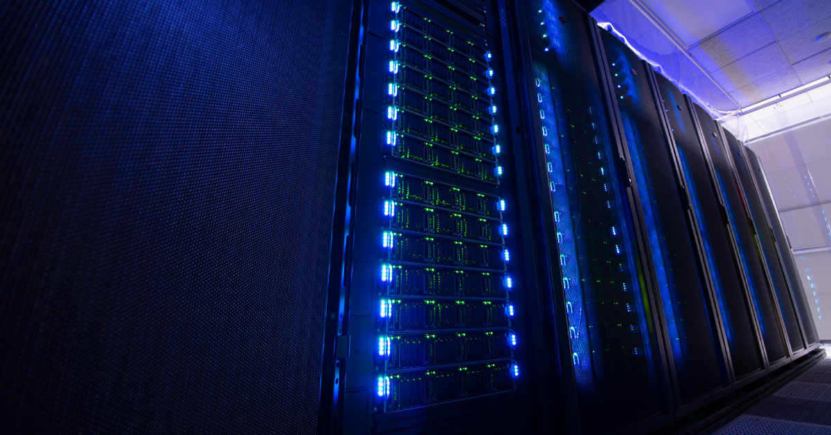 Rows of supercomputer server racks in a dark data center, illuminated by glowing blue and green LED status lights.